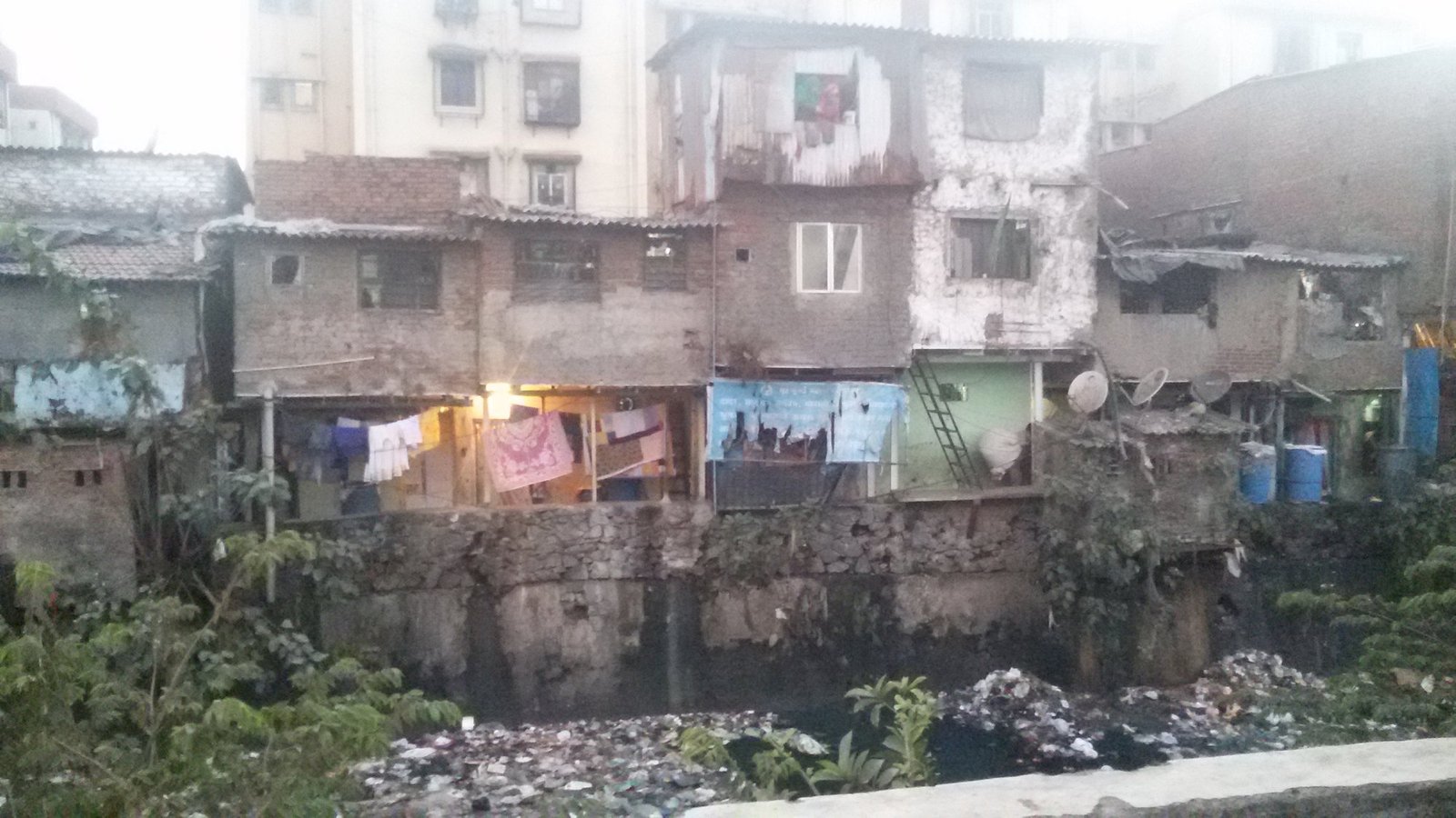 Dharavi homes above an open drain, with a new apartment block behind, 2015